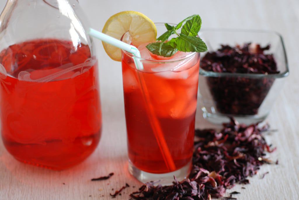Hibiscus flower Drink a pticher and glass filled with ice and the ruby red drink surrounded by dried hibiscus flowers