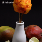 A mango on a stick, cut to look like a flower in a vase with chili and lime.