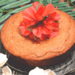 a round banana cake witha hisbiscus flower on top for decoration.