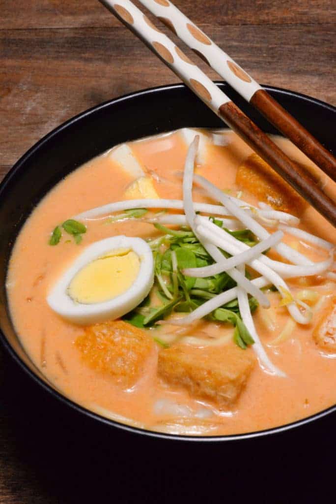 A picture of Malaysian Laksa a coconut curry soup garnished with bean sprouts, peas sprouts and sliced egg. 