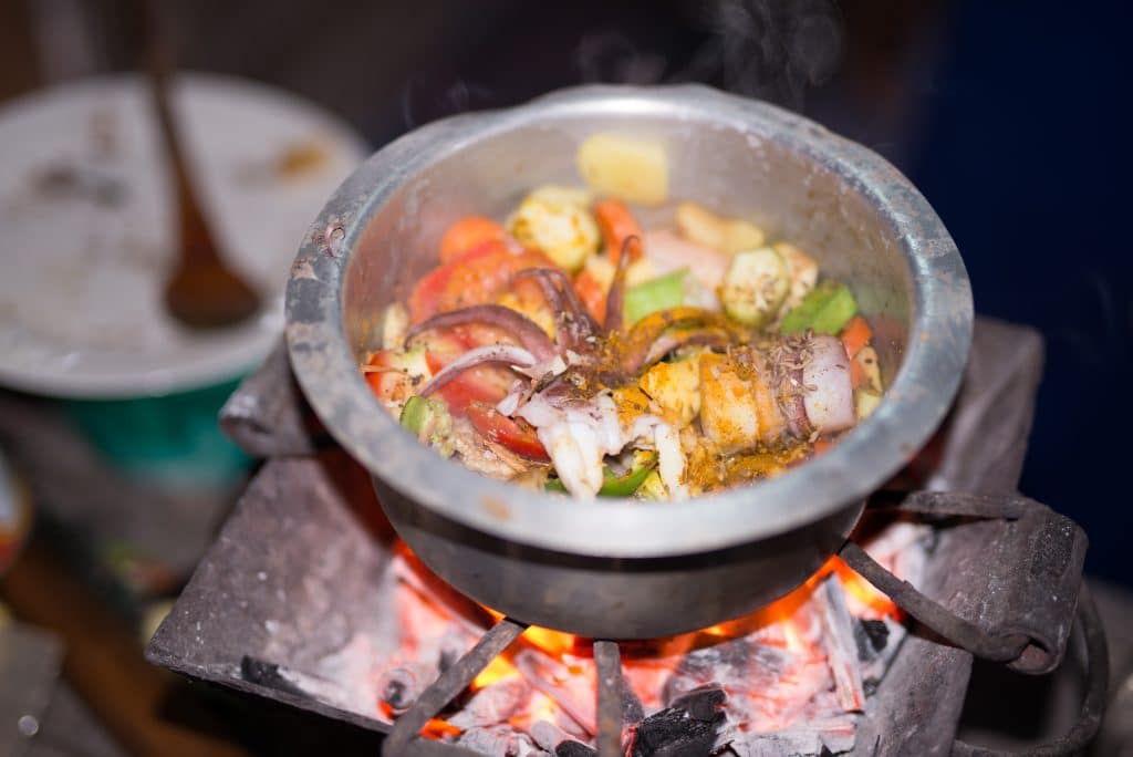 A pot of calamari curry cooking over charcoal