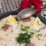 a bowl of polish white borscht soup garnished with eggs, dill, and grated fresh horseradish