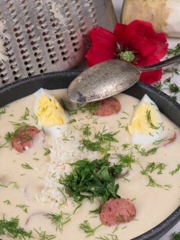 a bowl of polish white borscht soup garnished with eggs, dill, and grated fresh horseradish