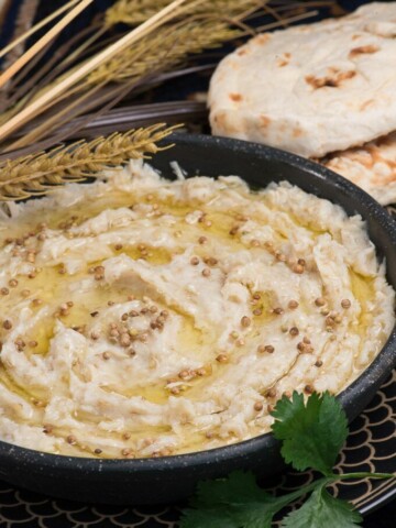 a creamy bowl of qatari harees that is drizzled with ghee and coriander seeds.