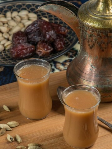 two cups of milky qatari karak tea surrounded by cardamom pods