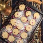 A cookies sheet ful of beautiful ma'amul cookies covered with powdered sugar and rose petals.