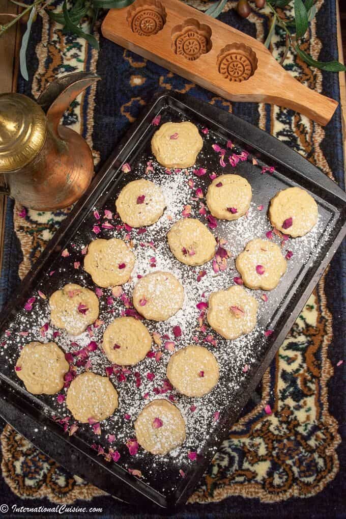 A cookies sheet ful of beautiful ma'amul cookies covered with powdered sugar and rose petals.