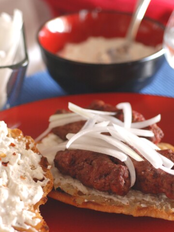 A picture of Serbian flat bread, topped with kaymak, cevapi, and onions.