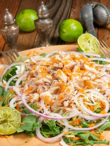a big plate of smoked fish salad with onions, carrots, cabbage on a bed of arugula