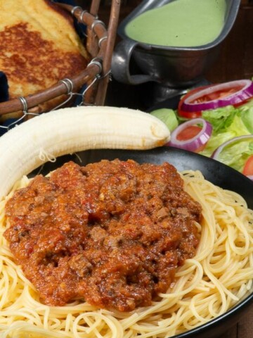 A plate full of pasta topped with Somali Pasta sauce called suugo along with a banana.