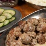 A plateful of swedish meatballs served with mashed potatoes, lingonberry sauce and cucumber salad.