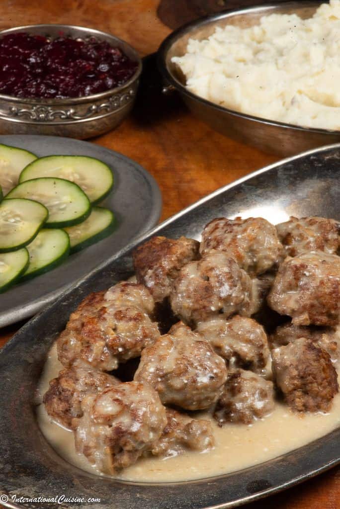 A plateful of swedish meatballs served with mashed potatoes, lingonberry sauce and cucumber salad. 