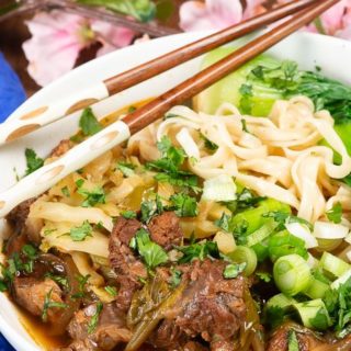 A bowl of Taiwanese beef noodle soup with chopstickes and plum blossoms