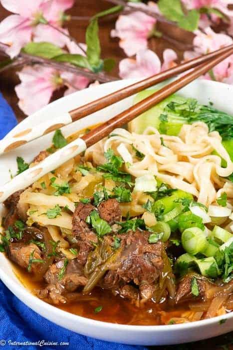 A bowl of Taiwanese beef noodle soup with chopstickes and plum blossoms