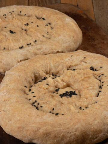 Two loaves of Tajik Bread which are round with sprinkling of black sesame seeds on top.