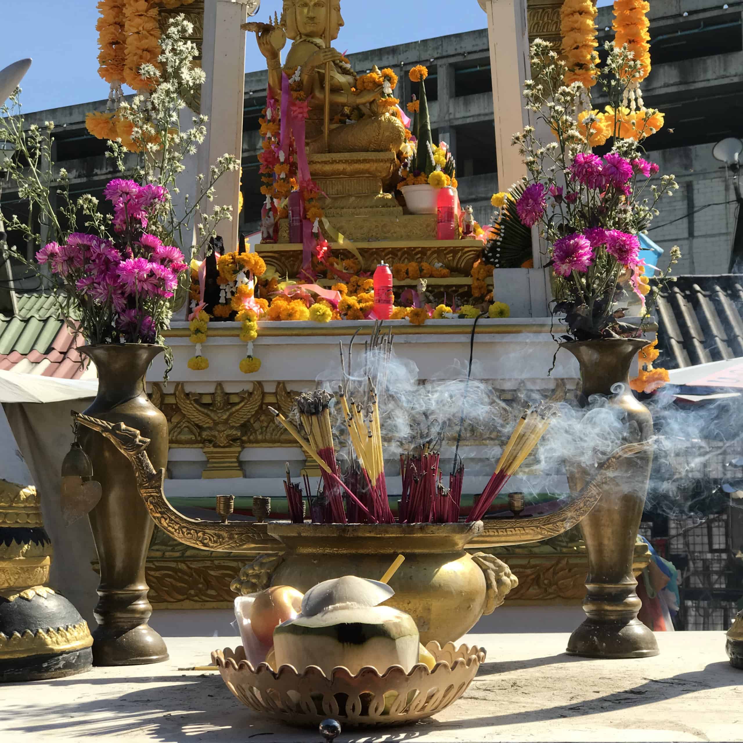 a spirit house at the weekend market filled with flowers, incense and candles.