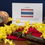 A menu with the Thai flag and symbols of Thailand a wooden boat, buddha statue, an elephant candle holder, a coconut and some Thai chilies.