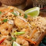 a plate full of Pad Thai stir fried noodles with shrimp and garnished with peanuts and lime wedges.