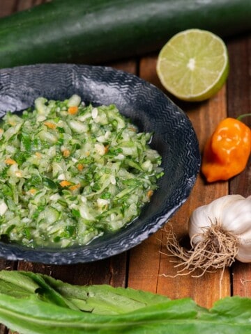 a bowl full of chadon beni sauce with ingredients on the side cucumber, lime, habanero, garlic and culantro.
