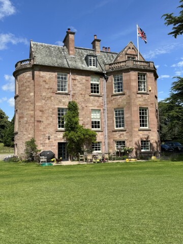 A beautiful manor made of red bricks surrounded by a huge green lawn.