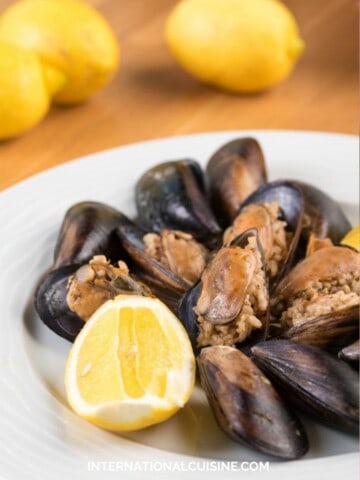 a plate full of Turkish stuffed mussels served with a slice of lemon.