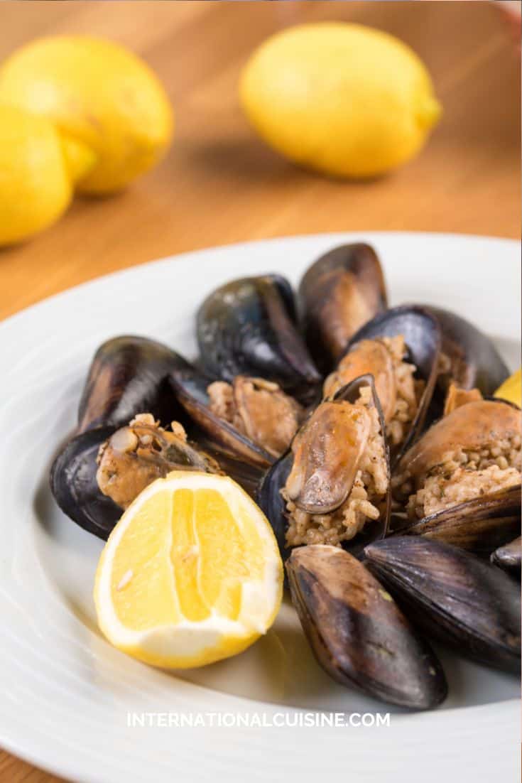 a plate full of Turkish stuffed mussels served with a slice of lemon.