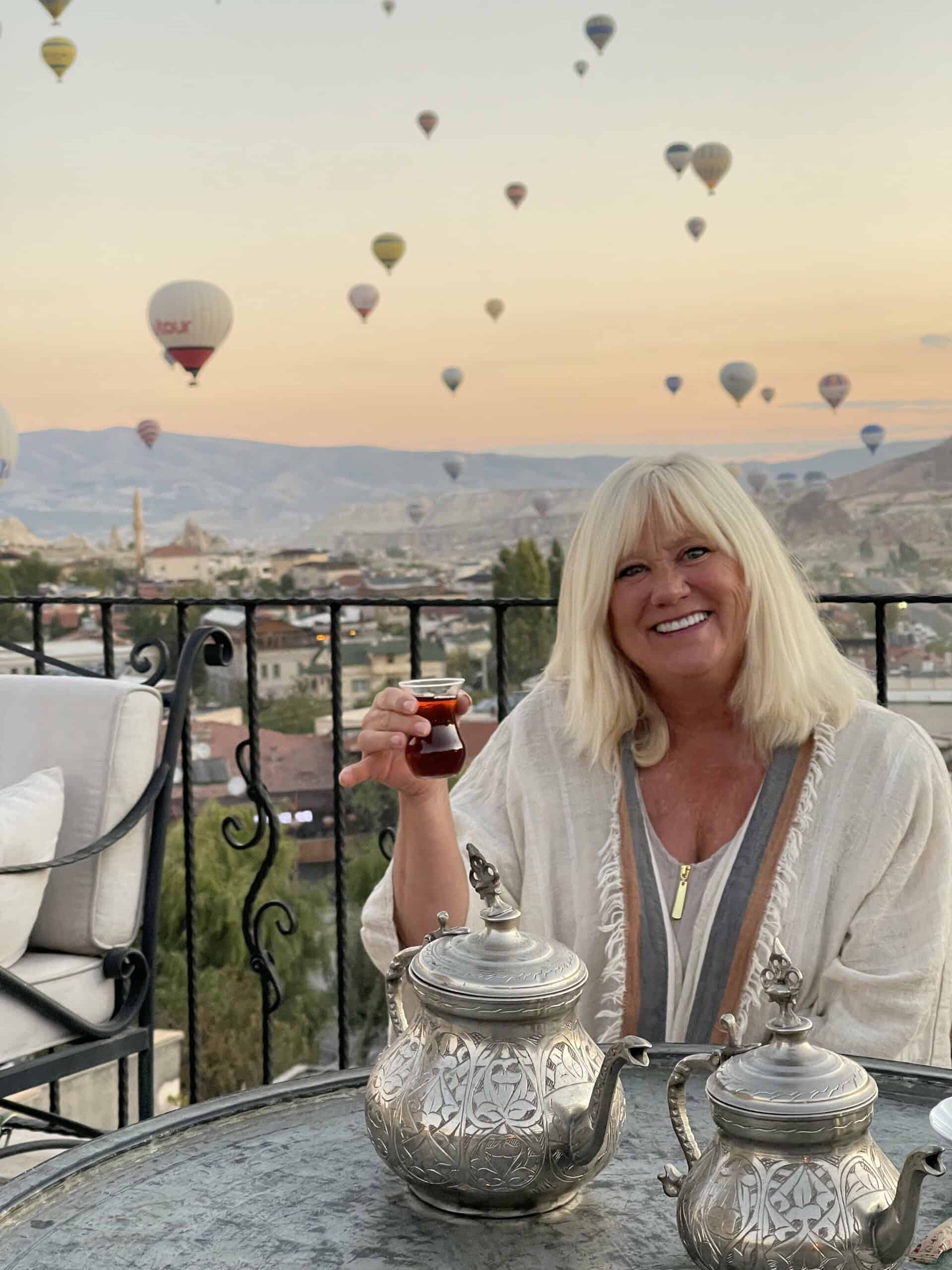 Having a cup of Turkish Tea on a balcony in Cappadocia with dozens of hot air balloons in the background.