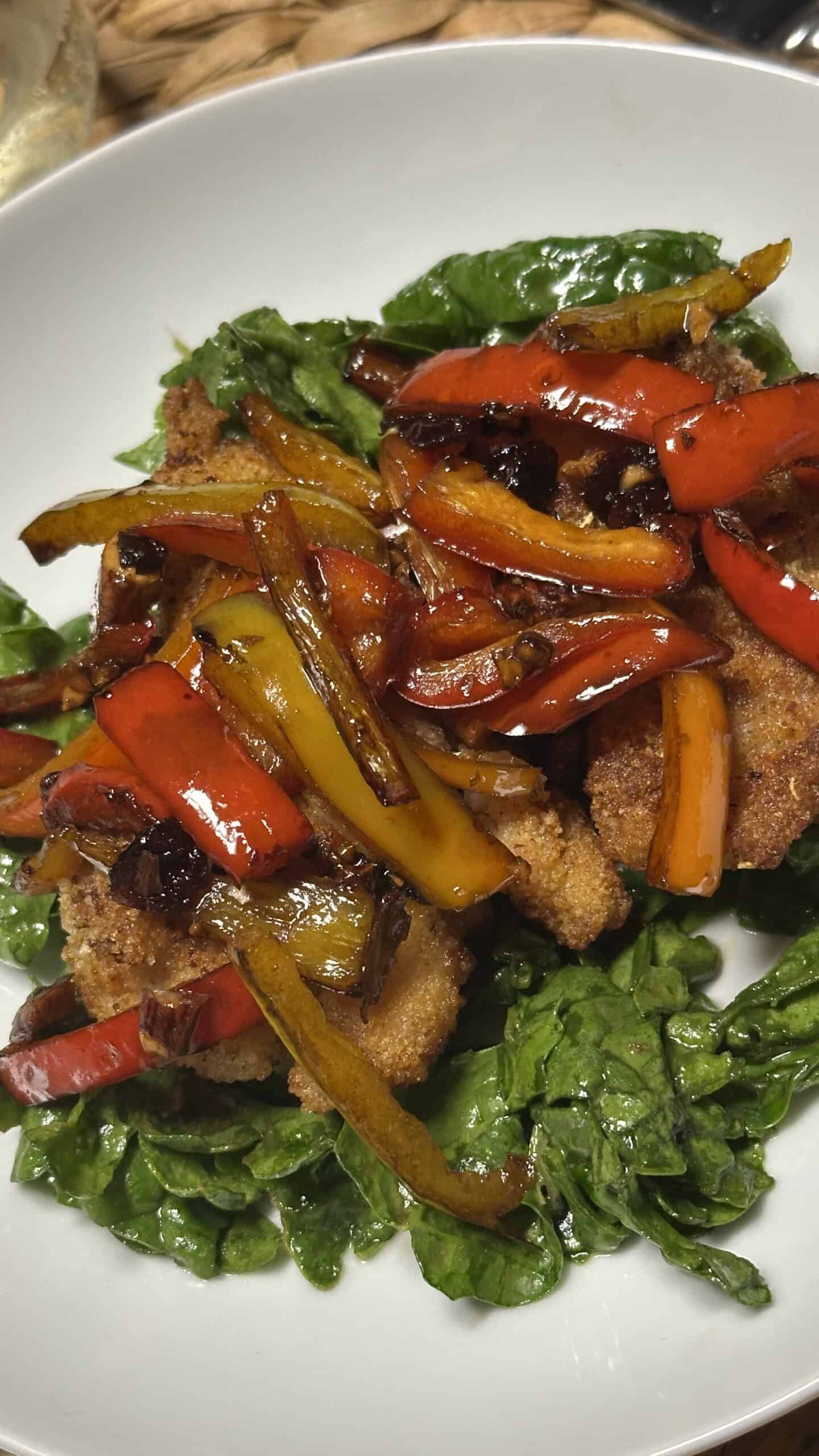 Chicken topped with colorful sautéed red and yellow peppers served over greens at a Sicilian dinner.
