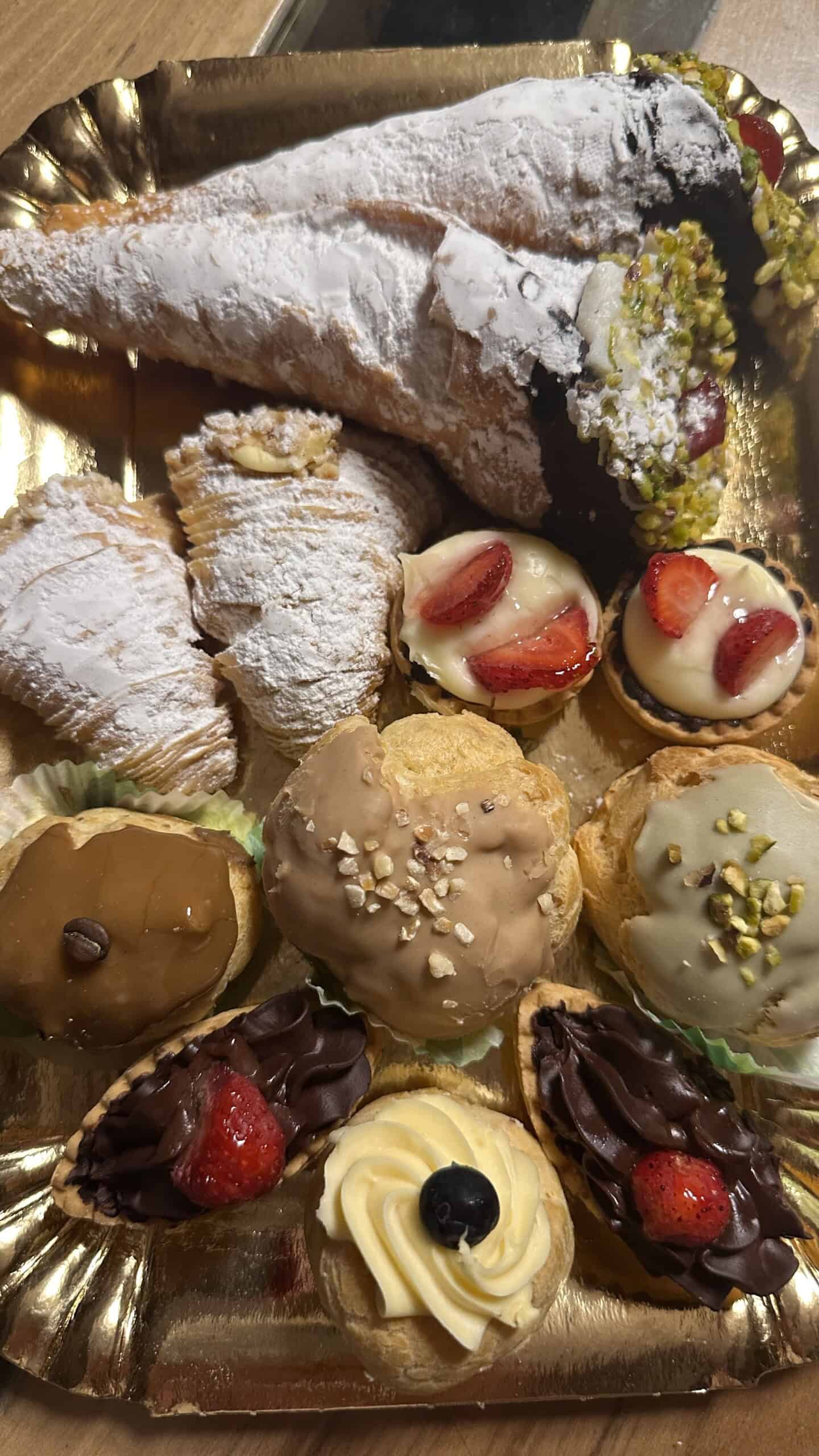An assortment of Sicilian pastries and sweets arranged on platter, including filled pastries and decorated desserts.