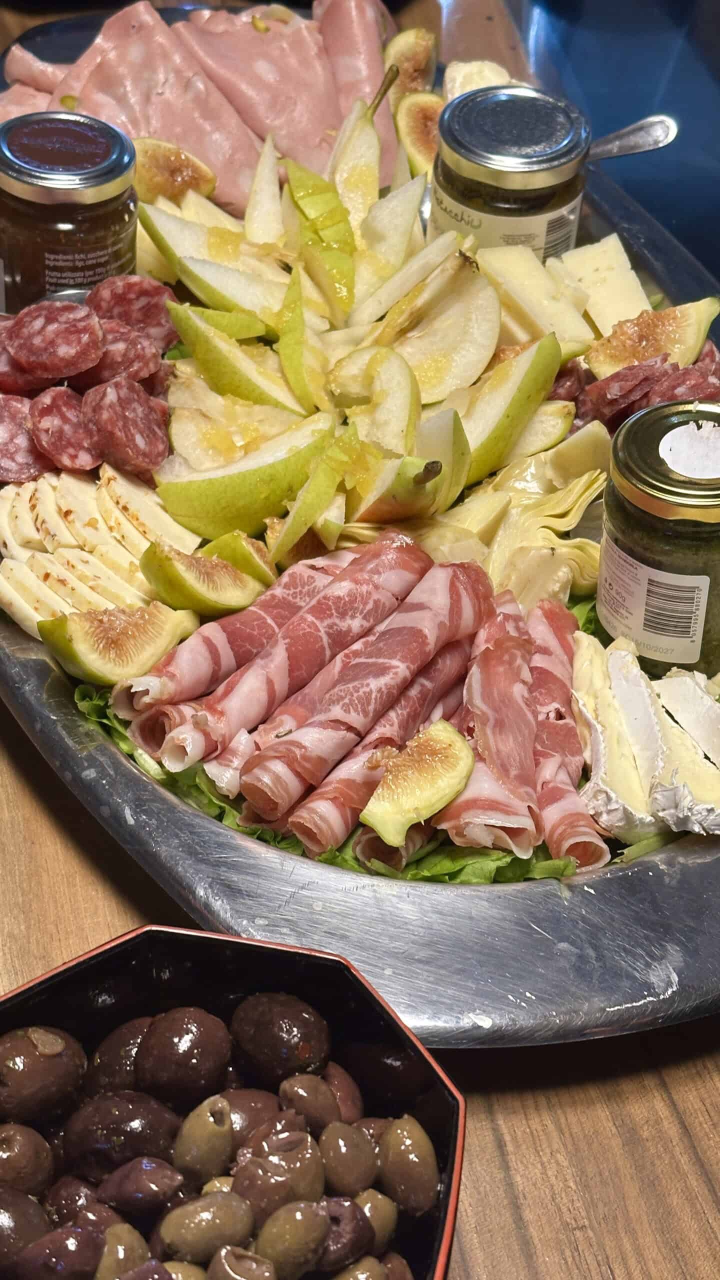 a plate full of Sicilian meats cheeses, figs and pears with jams, artichokes and olives.